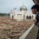Seorang warga menyaksikan kayu-kayu yang bertumpuk karena terbawa banjir di Pesantren Darul Mukhlisin, Aceh Tamiang, pada Minggu (14/12/2025). (Foto: Yasuyoshi CHIBA/AFP via Getty Images).